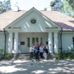 DSC_4319 Na obrazku widać grupę ludzi stojących przed białym pojazdem z kolumnami i dwuspadowym dachem, wyposażonym w zieleń. Plastikowa, malownicza sceneria, klasyczna architektura architektoniczna motywy.