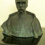 DSC_4334 Na obrazku pojawia się popiersie mężczyzny z wąsami, ubranego w szczegółowo wyrzeźbiony mundur, który jest wyświetlany jako medale. Popiersie jest eksponowane na tle jednolitego tła.