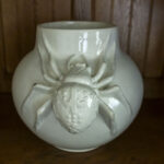 DSC_4341 Na obrazku znajduje się biała ceramika, która jest dostępna z przodu, jest to szczegółowa rzeźba pająka. Możliwość zastosowania stoi na drewnianej powierzchni, co stanowi wprowadzenie kontrastu dla podstawowej ceramiki i realistycznie uformowanego arachnida.