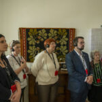 DSC_4344 Na ekranie pojawia się grupa osób stojących w pomieszczeniu, wszyscy noszą audioprzewodniki i słuchają. W tle na ścianie wisi kolorowa tkanina z zabezpieczeniem.