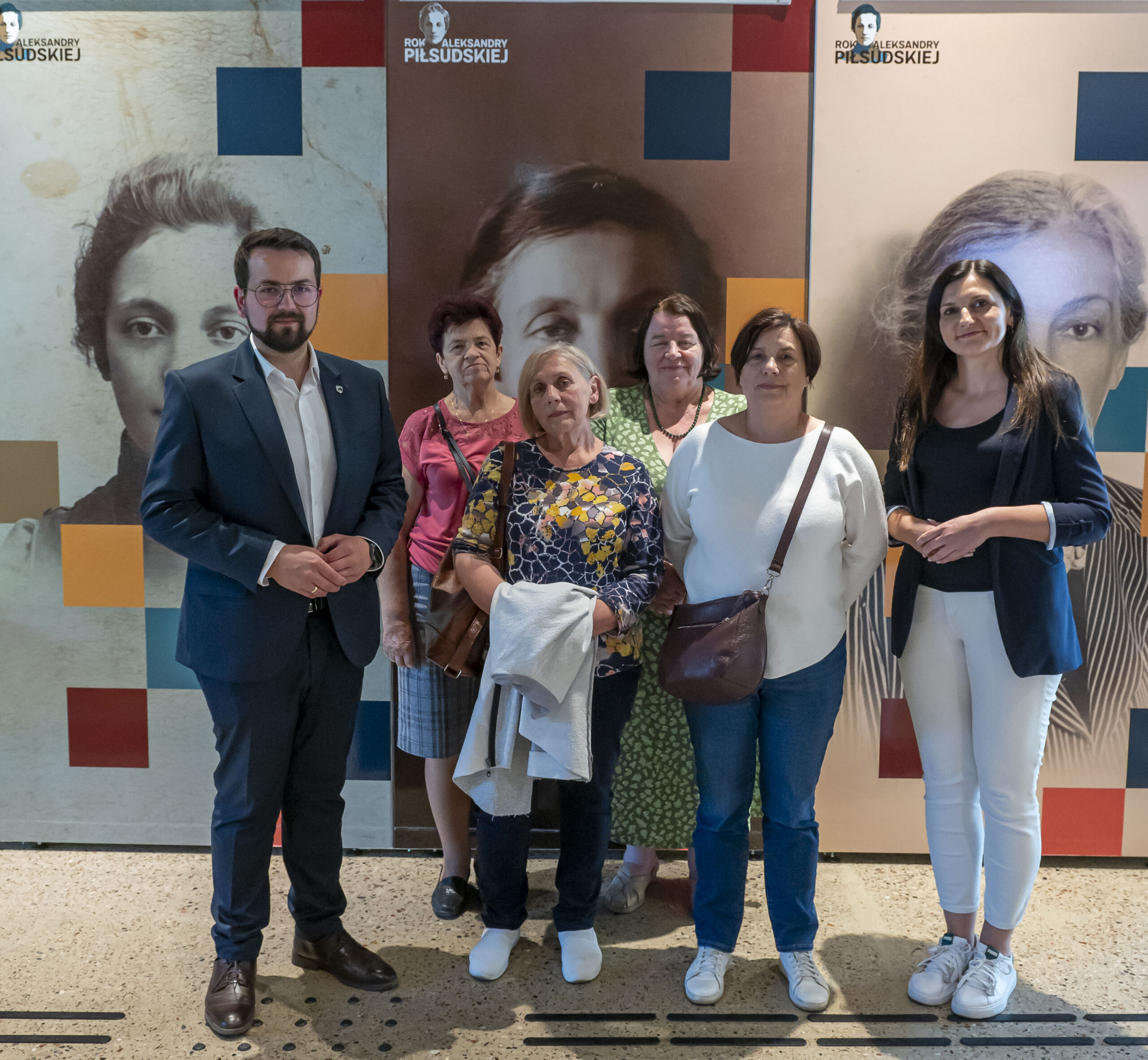 Na obrazku widać grupę sześciu osób, w tym cztery kobiety i dwóch mężczyzn, którzy uwolnili się przed wystawą z historycznymi fotografiami. Tło specjalne muzealne lub wystawowe, a konkretna osoba jest przedmiotem zainteresowania, które są eksponowane na zdjęciami.