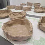 Na obrazku są widoczne wykonane miski z gliny w różnych stadiach końcowych, umieszczone na stole. Na ich powierzchni można zastosować różne detale tekstur.