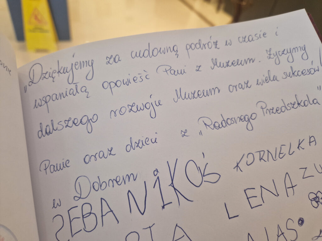 Przedstawione poniżej plan pisanej notatki w języku polskim na stronie zeszytu, wyrażającej się i dobre życzenia. W tle widoczne są kolorowe rysunki.