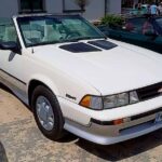 Na miejscu pojawia się biały Chevrolet Cavalier Z24 kabriolet ukryty na utwardzonej nawierzchni. Samochód ma czarny, składany dach oraz konstrukcję aerodynamiczną z charakterystycznymi otworami wentylacyjnymi na masce.