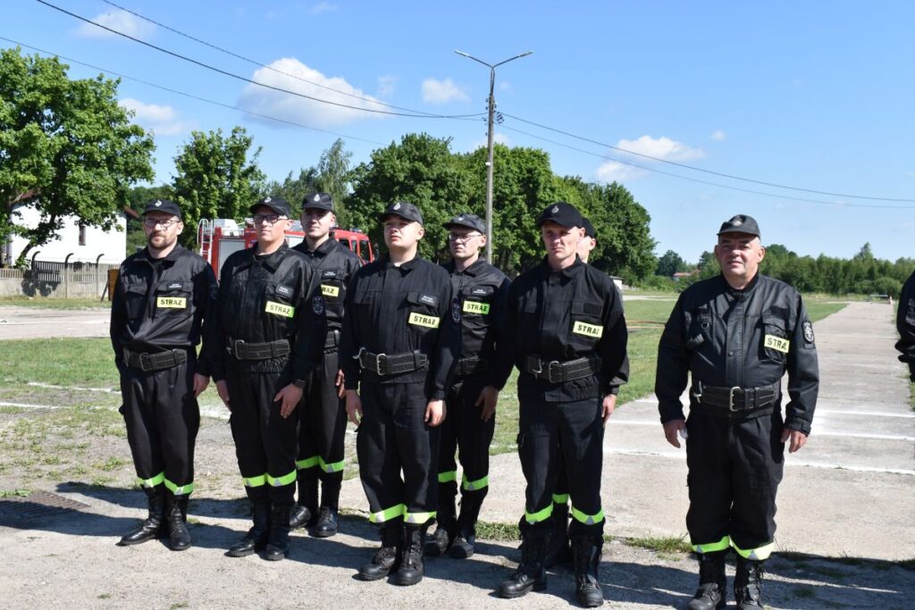 Na obrazie widocznym grupy osób w mundurach, które są uwalniane w rzędzie na świeżym powietrzu pod bezchmurnym niebem. W tle znajduje się drzewo oraz kilka budynków.