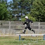 Na urządzeniu dostępnym w wyposażeniu biegowym po uderzeniu metalowej belce na zewnątrz, w granicach treningowej. W tle widoczne są drzewa oraz ogrodzenie.