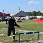 Na obrazie naturalnym w ekwipunku przeskakuje przez niebieską przeszkodę na trawiastym terenie podczas dziennego wydarzenia plenerowego. Całe zdarzenie wystąpiło w słoneczny dzień, na tle zielonej trawy i jasnego nieba.