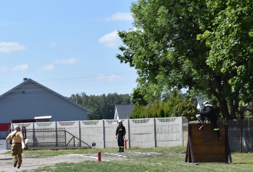 Na obrazie widocznym na szkoleniu; jeden drewniany wspina się po drewnianej ścianie, inny idzie w jej drodze, a trzeci raz w przebiegu ćwiczeń. Scena ma miejsce na świeżym powietrzu w pobliżu budynku i drzewa.