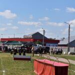 Na obrazie widocznym na zewnątrz z udziałem zgromadzonych w pobliżu chronionego schronienia sportowego oraz kilku namiotów. W tle są dostępne i bezchmurne niebo.