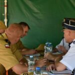 Dane dotyczące mężczyzn w mundurach wojskowych siedzących przy stole, na których znajdują się notatniki i butelki z wodą. W tle występuje zielone tło, a grupa jest zaangażowana w zasięgu.