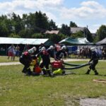 Na zdjęciu widać grupę usuwającą udział w ćwiczeniu z użyciem szkodnika na trawiastym terenie. Następujący ich ludzie są podporządkowani pod namiotami i zadaszeniami.