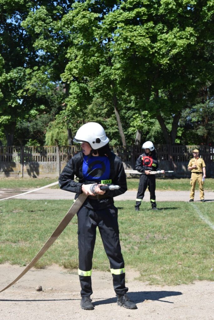 Na obrazach, które otrzymali podczas szkoleń, ubranych w stroje i kaski. Trzymają węże strażackie, ćwicząc na tle drewna i drewnianego ogrodzenia.