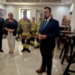 20240801_170958 Na obrazku mężczyzny w garniturze mówić przed grupą osób, wśród których znajdują się strażacy w mundurach. Pokój jest jasnooświetlony i wyposażony w oprawę zdjęć na ścianach.