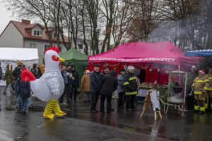 Na obrazku widać osobę w ciąży, która przechodzi obok zdarzenia na pokładzie. W tłumie są również strażacy, a nad pobliskim miejscem spalania unosi się dym, co dokładnie oczyszczanie na świeżym powietrzu.