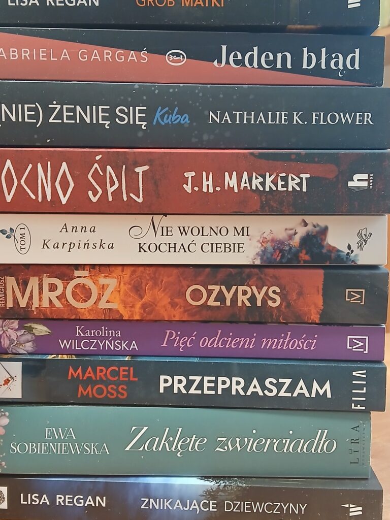 Na stosie znajduje się kilka książek, które są zawarte w języku polskim, a na grzbietach znajdujących się w tytułach i autorze publikacji. Książki są przedmiotem zainteresowania czytelników.