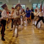 480564498_662747336100791_2728392790502174055_n Na obrazku widać dzieci ubrane w strojach tańczących w pokoju, podczas gdy występują ich występy. Kobieta w niebieskiej sukience prowadzi dzieci, otrzymując im w choreografii.
