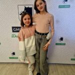 Na zdjęciu znajdują się dwie młode dziewczyny przed napisem „Gmina Dobre”. Obie sobie na sobie codzienne ubrania, a na tle logo przedstawiające świat dzika.