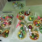 Na ekranie znajduje się element dekoracyjny, który jest dostępny w koszykach, wyposażony w kolorowe mi, owinięte w folię czekoladowe jajkami oraz miniaturowe kurczaczkami. Każdy z tych elementów jest przewiązanymi żywymi wstążkami, tworzącymi świąteczną atmosferę.