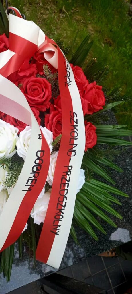 Bukiet czerwonych i białych róż z zielonymi liśćmi. Na wstążce czerwono-białej widnieje napis. Tło jest zielone i czarne.