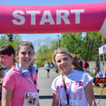 Grupa biegaczy przy starcie maratonu. Nad nimi różowy łuk z napisem START. Tło zielone drzewa i niebo.