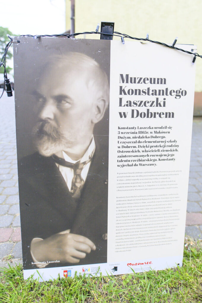 Portret mężczyzny na planszy informacyjnej z tekstem o Muzeum Konstantego Laszczki w Dobrem. Obraz czarno-biały; tło jasne. Na dole widoczne logotypy instytucji.