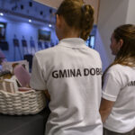 Dwójka dzieci w białych koszulkach, z napisami Gmina Dobre. Na blacie kosz z przedmiotami, w tle galeria.