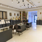 Wnętrze muzeum z wystawą popiersi na ciemnych postumentach. Ściany w beżach, sufit z jasnymi reflektorami. W tle ozdoby kwiatowe.