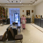 Muzealna sala z popiersiami na ciemnych postumentach. Kobieta w różowym stroju na jasnej podłodze. Kolorowe dekoracje na ścianie.