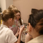 Grupa dzieci ogląda koszyk z przedmiotami w jasnym pokoju. W tle widoczna rzeźba i beżowa ściana. Jedno z dzieci trzyma pudełko.