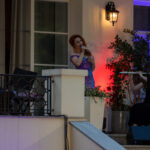 Trzyosobowy zespół muzyczny gra na scenie. Kobieta w fioletowej sukni śpiewa, obok pianista i flecistka. Tło oświetlone na czerwono.