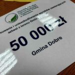 Certyfikat na białym tle przedstawia dotację 50 000 zł dla Gminy Dobre. Logo z zielonym liściem u góry. Stoi na drewnianym stole.