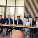 Grupa ludzi siedzi za długim stołem w sali konferencyjnej. Tło z drewnianymi panelami, godła na ścianie. Elegancka atmosfera spotkania.