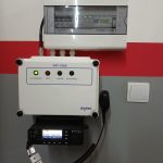 Białe urządzenia elektryczne na ścianie. Czerwono-szare tło z włącznikami i kablami. Zielona i czerwona dioda na panelu.