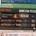 Stos książek z różnobarwnymi grzbietami, od żółci, przez zieleń, po róż. Każda książka ma widoczny tytuł i autora. Tło jest białe.