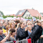 Na zdjęciu tłum ludzi na koncercie. W tle widoczne są domy z kolorowymi dachami. Ubrania osób są różnobarwne.