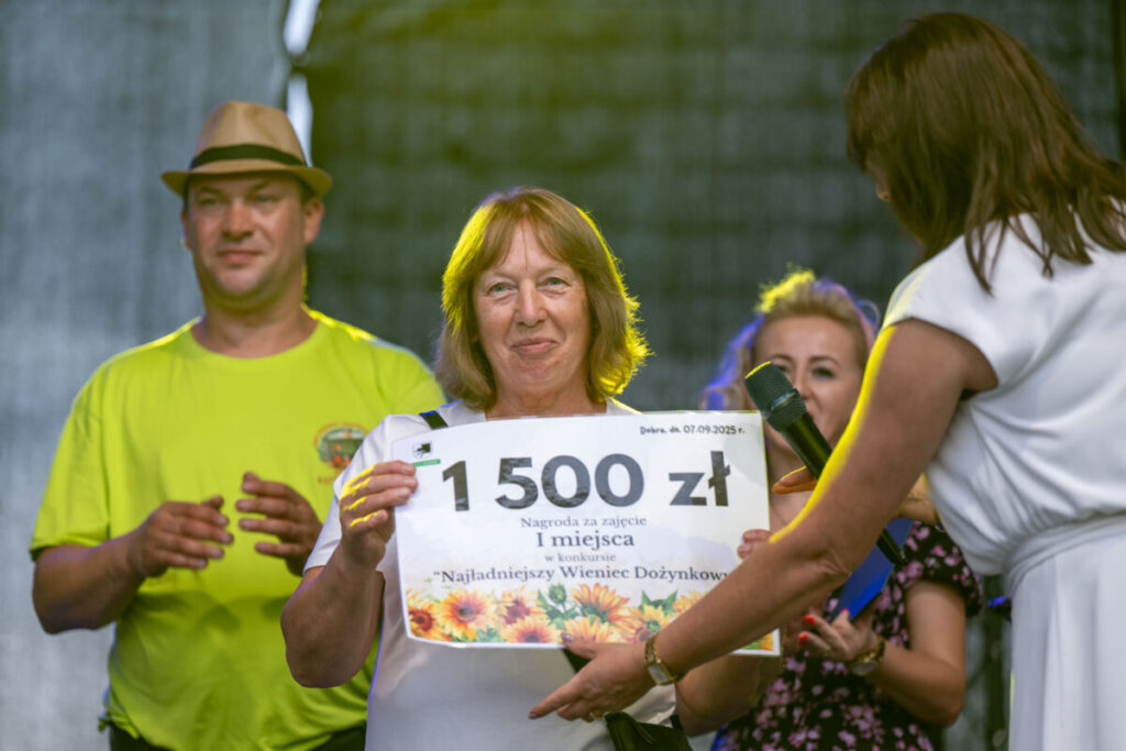 Na zdjęciu kobieta z nagrodą 1500 zł, z jasnym tłem. Obok niej dwie osoby, jedna w jasnej koszulce.