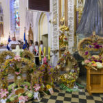 Ołtarz w kościele z dożynkowymi wieńcami z kwiatów i zbóż. Kolorowe kwiaty i złote elementy. Tło z freskami i witrażem.