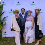 Grupa czterech osób pozuje na tle ścianki z logiem Gminy Dobre. Mają na głowach wianki, a tło zdobią zielone rośliny. Zdjęcie wykonane jest na zewnątrz, na trawie.