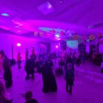 Sala przyozdobiona dyniami na suficie, wypełniona bawiącymi się ludźmi w kostiumach. Różowe oświetlenie tworzy nastrojową atmosferę. W tle widać siedzących gości.