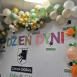 Na zdjęciu dekoracja z balonów w odcieniach zieleni, złota i bieli. Napis Dzień Dyni na białym tle. Ozdobne elementy przedstawiają dmuchane dynie.