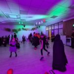 Dzieci w przebraniach na przyjęciu Halloween. Fioletowe i zielone oświetlenie. Ściany ozdobione balonami i dyniami.