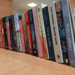 553777438_1219292926687997_7793563312790575620_n Na zdjęciu widać rząd książek ustawionych pionowo na drewnianym blacie. Okładki są kolorowe, a w tle znajduje się jasna ściana. Oświetlenie jest jasne, prawdopodobnie sztuczne.