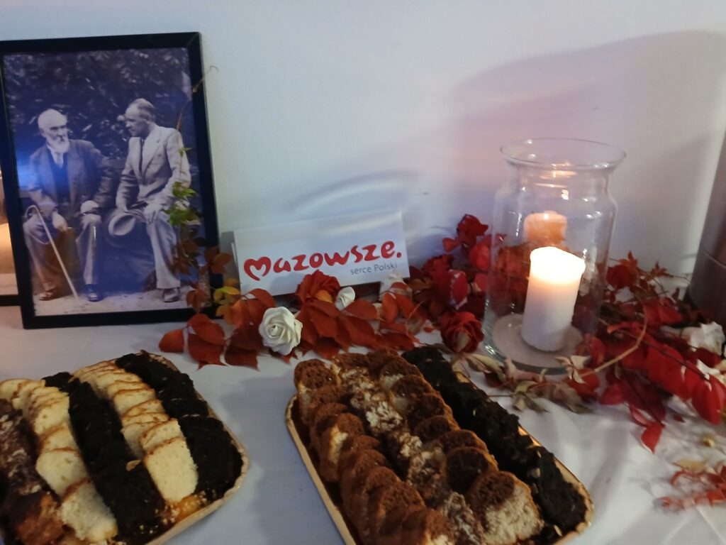 Przedszkolaki siedzą na kolorowych poduszkach i oglądają książki przed nimi leży kilkanaście misiów pluszowych w tle czarna kotara z białym napisem