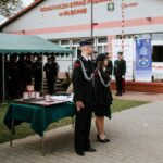 8TVU1VNo Ceremonia przed strażnicą OSP w Mileńcu, ludzie w mundurach. Na pierwszym planie stół z nagrodami, w tle namiot i budynek.