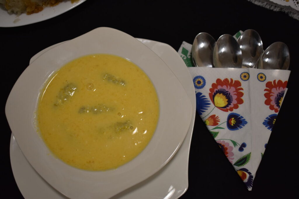 Talerz z żółtą zupą na białym talerzu, obok kolorowa serwetka z łyżkami na ciemnym tle.