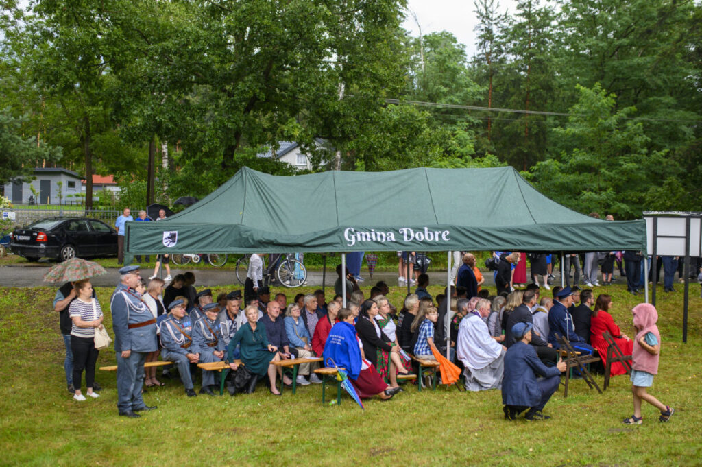 Na zdjęciu jest zielony namiot z napisem Gmina Dobre. Pod namiotem siedzą ludzie. W tle widać drzewa i rowery.