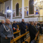 Kościół wypełniony ludźmi w różnorodnych ubraniach, z flagami. Ściany zdobią malowidła religijne. Widoczne żyrandole i ławki.