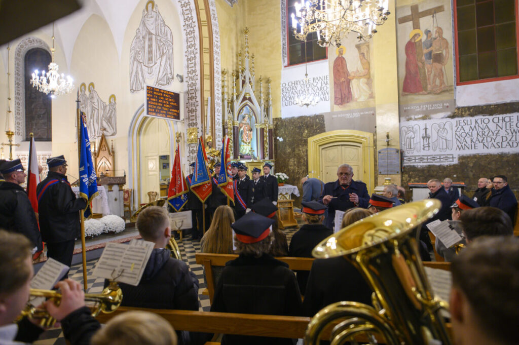 Ceremonia w kościele, z flagami i orkiestrą dętą. Wnętrze ozdobione freskami i żyrandolami. Uczestnicy w mundurach.