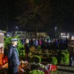 Pomnik Józefa Piłsudskiego otoczony wieńcami. W tle noc i tłum ludzi. Harcerze i żołnierze stoją obok pomnika.