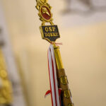 Sztandar z napisem OSP Dobre w złotych i czerwonych barwach. Tło jest rozmyte w odcieniach beżu. Przy sztandarze widoczne biało-czerwone wstęgi.